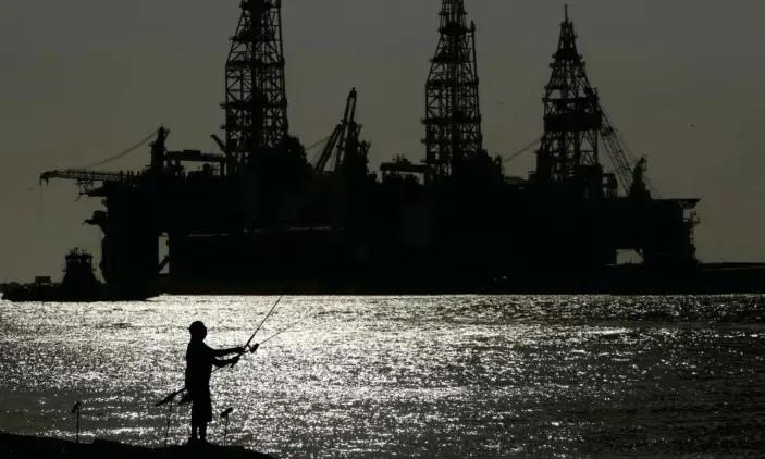  ?? Photograph: Eric Gay/AP ?? A man fishes near docked oil drilling platforms in Port Aransas, Texas.