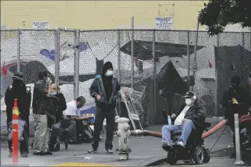  ?? ASSOCIATED PRESS ?? PEOPLE LINGER ON A STREET CORNER on Saturday. in front of tents set up in a fenced lot in San Francisco