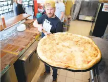  ?? STEPHEN M. KATZ / STAFF ?? Benny Cavalloni’s co-owner Chris Brown removes one of the restaurant’s signature 28-inch pies from the oven of their newest location at Virginia Beach’s Town Center last week.
