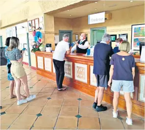  ??  ?? Receptioni­sts in face masks at the H10 Costa Adeje Palace in Tenerife deal with guests confined to the building and its grounds, while police outside erect barriers to restrict arrivals and departures
