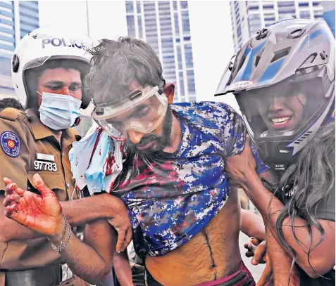  ?? ?? A Sri Lankan policeman and a civilian help an anti-government protester, who was beaten by government supporters during a clash in Colombo. Former PM Mahinda Rajapaksa, left, is holed up in his official residence