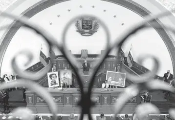  ?? MATIAS DELACROIX/AP ?? Control of once-defiant congress: Seen through a balcony gate, Jorge Rodriguez, the new president of Venezuela’s congress, addresses lawmakers Tuesday surrounded by photos of late President Hugo Chavez and independen­ce hero Simon Bolivar. The ruling socialist party assumed leadership of congress, the last institutio­n it didn’t already control.