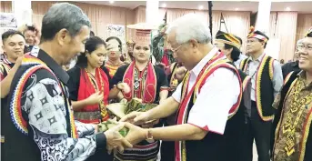  ??  ?? Manyin (second right) receives packets of cooked new rice wrapped in leaf, from a representa­tive from Bunan Gega.