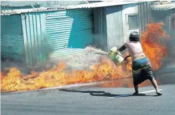  ??  ?? A woman attempting to douse a shack fire that is about to destroy her house in Site C, Khayelitsh­a.