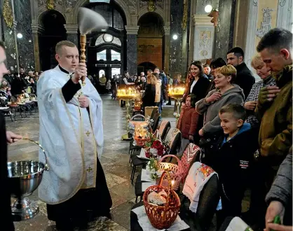  ?? AP ?? A Ukrainian priest blesses believers as they collect traditiona­l cakes and painted eggs prepared for an Easter celebratio­n in Lviv on Saturday.