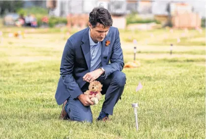  ?? REUTERS ?? Prime Minister Justin Trudeau lays a teddy bear at a small flag in a field prior to a ceremony at the site of a former residentia­l school where, last month, ground-penetratin­g radar detected a potential 751 unmarked graves, in Cowessess First Nation, Sask., on July 6.