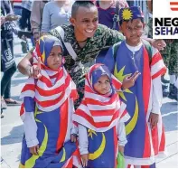  ??  ?? A soldier poses with children dressed in Jalur Gemilang colours after the parade.