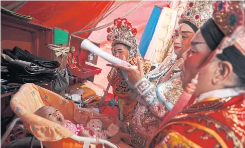  ?? PHOTO: PATIPAT JANTHONG ?? TOUGH AUDIENCE: A baby born to a Chinese opera performer yawns as colleagues check on her during a break at Talat Noi on Yaowarat Road in Bangkok. The venue is crowded with visitors paying their respects to deities to mark the nine-day Vegetarian...