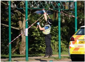  ??  ?? A police officer jumps to put tape on exercise equipment at Roath recreation ground in Cardiff after a man was seen using the equipment