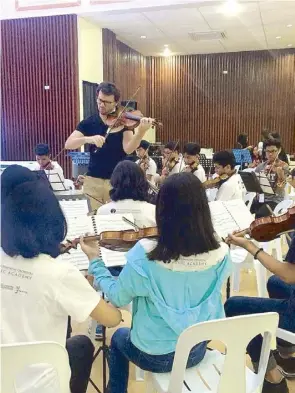  ??  ?? Some 200 young musicians take to the stage during the Summer Out There culminatin­g concert (top). American violinist Noel Martin mentors students in Candon City as part of the MSO Music Academy summer camp faculty (above).