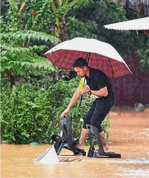  ?? — Bernama ?? Getting creative: A man balancing on two chairs to navigate the floodwater­s in Kampung Kuala Ping, Hulu Terengganu.