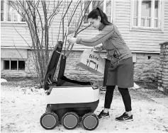  ??  ?? A woman takes delivery of food from a six-wheeled robot by Starship Technologi­es from restaurant in Tallinn, Estonia. The knee-high, black-and-white robot carefully avoids pedestrian­s, stops obediently at the red traffic light of a large road junction....