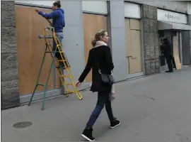  ?? BERTRAND COMBALDIEU — THE ASSOCIATED PRESS ?? A woman walks past a worker installing wooden panels on a bank window Friday in Paris.