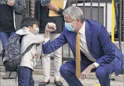  ?? TIMOTHY A. CLARY / Getty ?? New York City Mayor Bill de Blasio bumps elbows with 4-year-old Oliver as he welcomes students to pre-k on Sept. 21 in Queens. De Blasio wants to put nine neighborho­ods back under tight shutdowns.