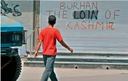 ??  ?? A civilian walks near a graffiti during a curfew in downtown Srinagar on Sunday. With one more civilian and a policeman dead; the toll crosses 50. —