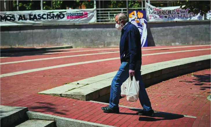  ?? ALBERTO R. ROLDÁN ?? Un hombre pasa con la compra delante de una pancarta contra el fascismo, en la «Plaza Roja» de Vallecas