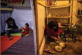  ?? (AP/Hassan Ammar) ?? Syrian refugee Ayesha al-Abed, 21, (right) prepares food as her husband, Raed Mattar, 24, (left) plays with their daughter Rayan before they break their fast April 13, first day of the fasting month of Ramadan, in a refugee camp in Tripoli, Lebanon.