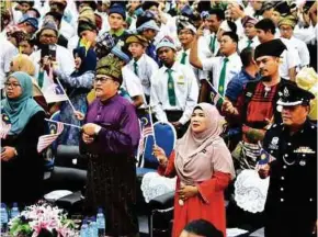  ??  ?? Radin Hashimah (berbaju kurung merah) dan Hasanuddin (berbaju Melayu ungu) menyanyika­n lagu patriotik sambil mengibarka­n Jalur Gemilang.