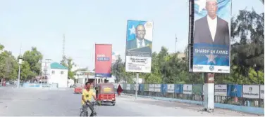  ?? Agence France-presse ?? ↑
A man cycles past election banners of presidenti­al candidates along a street in Mogadishu on Saturday.