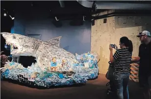  ??  ?? Children sit in part of a boat incorporat­ed into the statue of "Greta the Great White Shark" which is part of Angela Haseltine Pozzi's project "Washed Ashore: Art to Save the Sea."