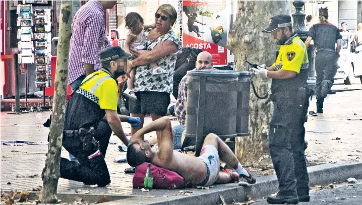  ??  ?? Police officers help the injured after a van crashed into pedestrian­s in Las Ramblas, downtown Barcelona. The area is popular with tourists and Britons spoke of running for their lives as the terror unfolded in one of the busiest areas of the Spanish...