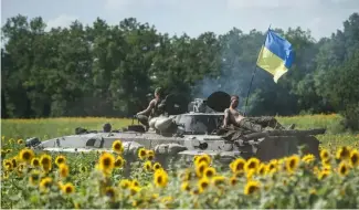  ?? ?? DOSSIER - Des troupes ukrainienn­es montent sur un véhicule blindé avec un drapeau ukrainien, dans un champ de tournesols à Kryva Luka, dans l'est de l'Ukraine, le samedi 5 juillet 2014.