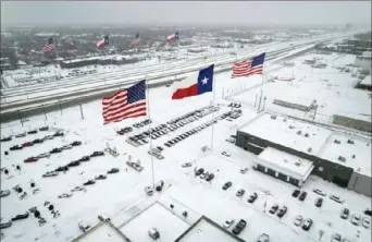  ?? John Moore/Getty Images ?? U.S. and Texas state flags fly over car dealership­s as light traffic moves through snow and ice on U.S. Route 183 on Thursday in Irving, Texas. A winter storm blanketed much of Texas with snow, sleet and freezing rain as it swept east, also affecting much of the Midwest and eastern United States.