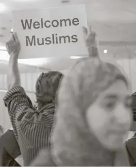  ?? Christian K. Lee / Los Angeles Times ?? A protester welcomes Muslims to the United States at Los Angeles Internatio­nal Airport on Thursday as a scaled-back version of President Donald Trump’s travel ban takes effect. Human rights groups plan to challenge the new rules.