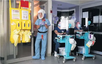  ?? JOHN J. KIM/CHICAGO TRIBUNE ?? Blessing Hospital nurse Michelle Summy disinfects her hands while exiting a COVID-19-positive patient’s room as two respirator­y therapists go over patient charts on computer monitors at the hospital’s intensive care unit on Thursday in Quincy.