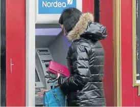  ?? /Bloomberg ?? Reliable: A customer uses an ATM operated by Nordea Bank in Riga, Latvia. Nordea, the biggest Nordic lender, has benefited from investor loyalty towards banks in the region.