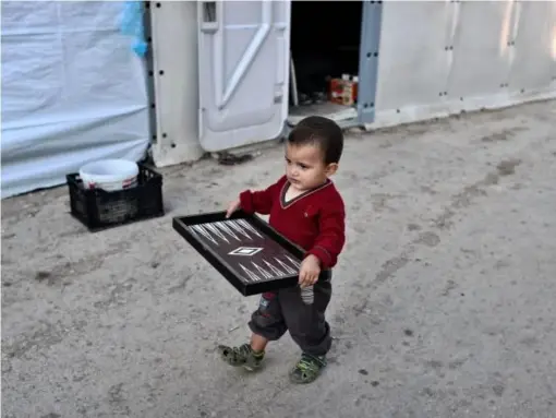  ?? (AFP/Getty) ?? A child carries a broken Backgammon game in a makeshift camp