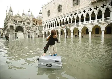  ?? LUCA BRUNO/AP ?? KOTA YANG BASAH: Seorang wisatawan mendorong kopernya yang mengambang di Lapangan Santo Markus, Venesia, kemarin.