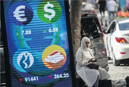  ?? YASIN AKGUL/AFP/GETTY IMAGES ?? A woman sits beside a digital billboard giving updates on various currencies and the Turkish stock exchange in Istanbul on Monday. The record plunge of Turkey’s currency, the lira, has raised concerns of a contagion hitting emerging economies.