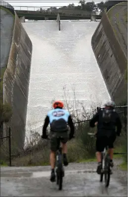  ?? ANDA CHU — STAFF PHOTOGRAPH­ER ?? Mountain bikers ride past the spillway at the Lexington Reservoir just south of Los Gatos on Saturday. As a result of recent storms, the reservoir filled to the top and began spilling over its spillway Friday into Los Gatos Creek.