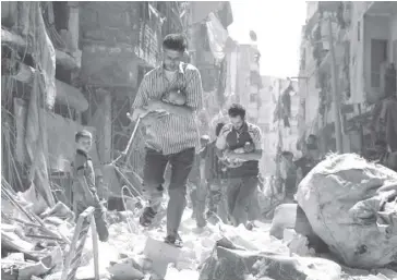  ?? NY TIMES ?? Syrian men carrying babies made their way through the rubble of destroyed buildings after a reported airstrike on a rebel-held neighborho­od in Aleppo, Syria.