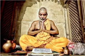  ??  ?? A Hindu pandit prays before starting his morning rituals on the banks of the river in Varanasi while reading the holy scriptures