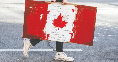  ?? PETER J THOMPSON / NATIONAL POST FILES ?? A protester walks up Toronto’s Bay Street holding a painted Canadian flag with names of people killed by police.