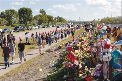  ?? Associated Press photo ?? Parents and students walk by the memorial for the victims of the shooting at Marjory Stoneman Douglas High School on Sunday for an open house as parents and students returned to the school for the first time since seventeen victims were killed in a...