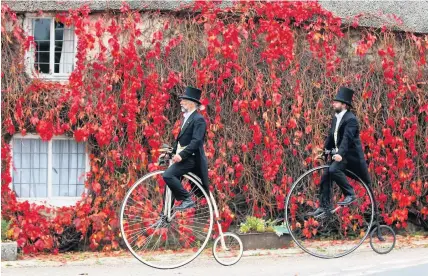  ?? Richard Austin ?? Alistair Cope and his son, Sebastian, prove that there are not many places you can’t cycle your Penny Farthing as they pass a Devon Long House in Whiteford, in East Devon, where autumn colours of brilliant red leaves cling to the outside of the building