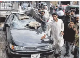  ?? AP ?? People stand near a car damaged from an earthquake in Peshawar, Pakistan. A powerful earthquake in northern Afghanista­n rocked cities across South Asia on Monday.