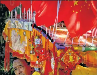  ?? AP PHOTO ?? A driver looks out from his trishaw decorated with an American flag and Chinese flags in Beijing on Sunday. Chinese news reports have quoted a former finance minister as saying Beijing can disrupt American companies’ operations by imposing “export controls” if it needs more leverage in its mounting tariff dispute with Washington.