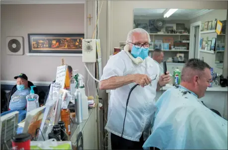  ?? THE ASSOCIATED PRESS ?? Karl Manke, 77, left, wears a mask while cutting hair May 5at Karl Manke’s Barber and Beauty Shop in Owosso, Mich. Manke re-opened his doors on Monday in defiance of Gov. Gretchen Whitmer’s executive order mandating salons, barbershop­s and other businesses to stay closed. He has already given nearly 100 haircuts, and fields more calls than that daily, all while continuing to cut hair.