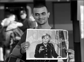  ?? MICHAEL PROBST / ASSOCIATED PRESS FILE (2015) ?? A refugee carries a picture of German Chancellor Angela Merkel on Sept. 5, 2015, as he arrives at the main train station in Munich, Germany.