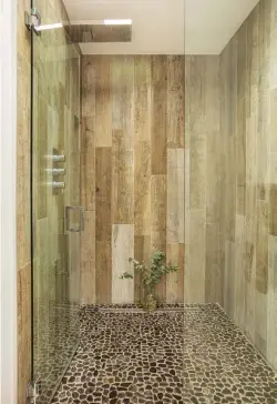  ?? ?? ABOVE, RIGHT: IN A NOD TO MID- CENTURY “RUMPUS ROOMS,” AND TO CREATE A CONNECTION TO THE GEOMETRIC WOOD VANITY THAT’S PLACED OUTSIDE THE BATHROOM, FRANK CHOSE PORCELAIN TILE IN A WOOD PRINT. THE RIVER STONES USED IN THE BASE OF THE SHOWER ARE “LIKE A FOOT MASSAGE EVERY MORNING,” HE SAYS.