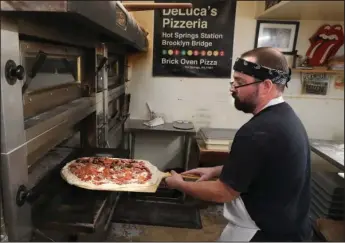  ?? The Sentinel-Record/Richard Rasmussen ?? ‘ABSOLUTE BEST’: Deluca’s Pizzeria employee Zach Nix slides a pizza into the oven on Thursday.