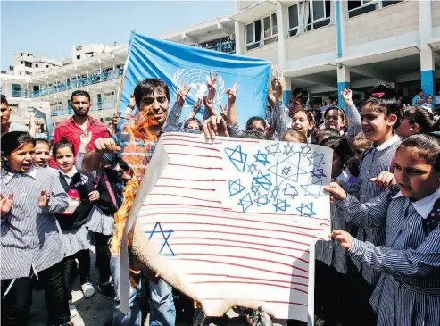  ?? HAZEM BADER / AFP / GETTY IMAGES ?? Palestinia­n schoolchil­dren burn a sign depicting a makeshift U.S. flag, with the Star of David replacing traditiona­l pentagrams in the canton, during a protest at a United Nations Relief and Works Agency (UNRWA) school last month.
