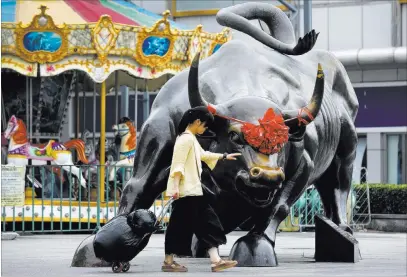  ?? Andy Wong ?? The Associated Press A woman pulling a two-wheel trolley loaded with goods touches a bull statue on display Monday outside a retail and wholesale clothing mall in Beijing. The trade war that erupted Friday between the U.S. and China carries a major...