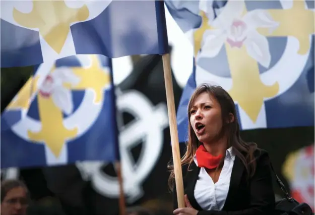  ??  ?? Les drapeaux à l'orchidée blanche sur une croix celtique, l'emblème des Caryatides, se mêlent désormais à ceux d'organisati­ons plus anciennes lors des manifestat­ions nationalis­tes. Sophie, 25 ans, arbore fièrement les couleurs du mouvement lors du défilé en l'honneur de Jeanne d'Arc, le 11 mai dernier, à Paris.
