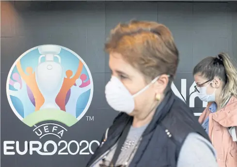  ?? REUTERS ?? People wearing protective face masks walk past the Euro 2020 logo in Romania before the tournament was postponed.