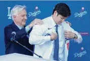  ?? Ashley Landis/Associated Press ?? The Dodgers’ Shohei Ohtani, right, puts on a jersey with the help of owner & chairman Mark Walter during a news conference at Dodger Stadium on Thursday.